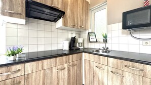 Une cuisine moderne avec des meubles en bois, un plan de travail noir, un four à micro-ondes encastré, une machine à café et une petite plante en pot.