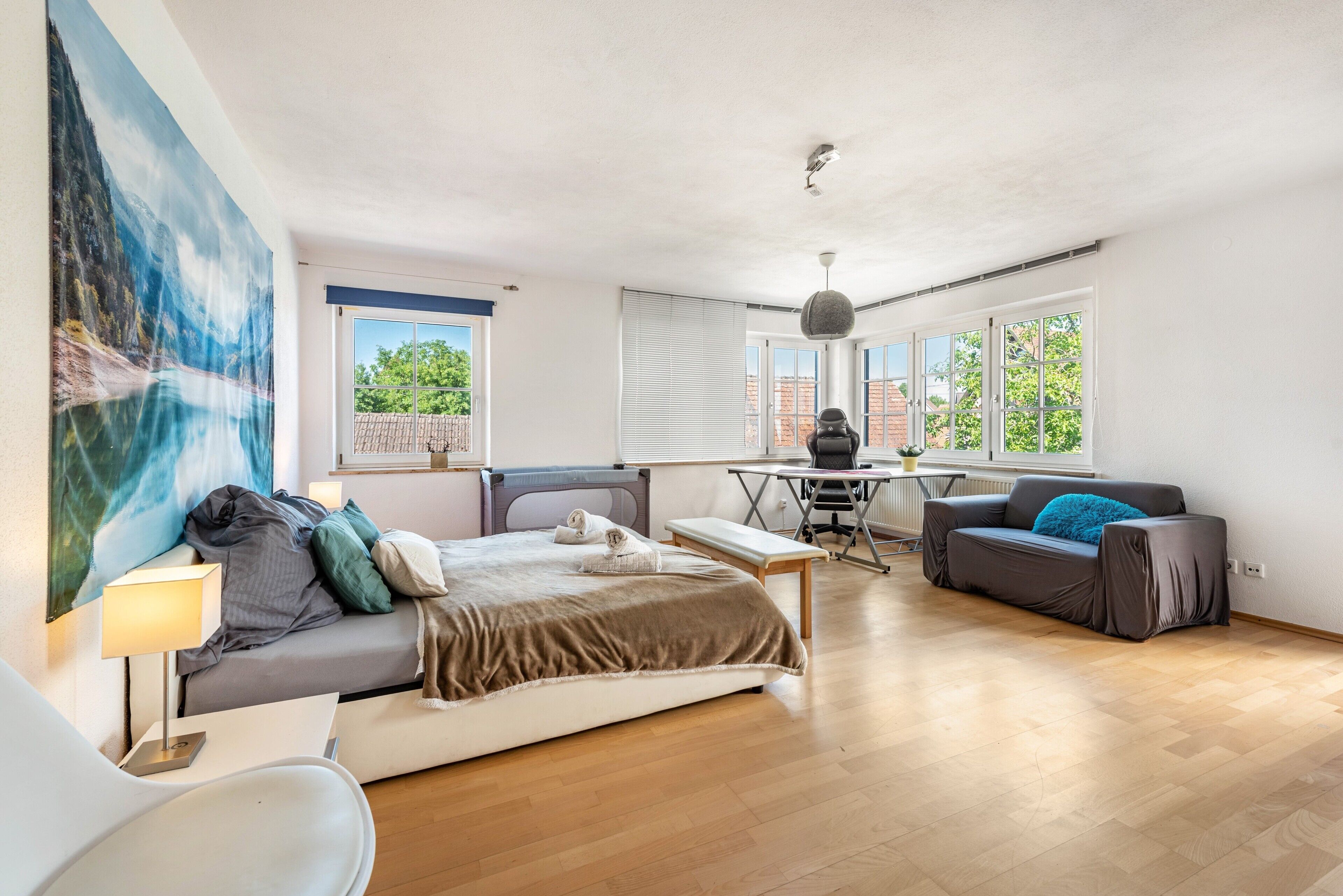 Una habitación amplia con cama, escritorio, sofá y ventanas grandes.
