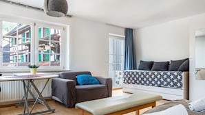 Quarto moderno com cama, um banquinho, uma mesa e janela com vista para edifícios.