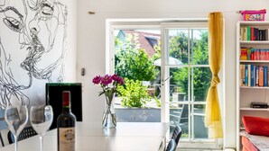 A dining table with wine glasses and a bottle, a vase with flowers, a bookshelf, and a view through a window. - Lake Constance Holiday Home Brunnenberg – Relaxation Close to the Lake (Sipplingen)