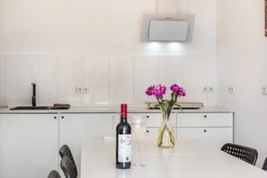 Eine moderne Küche mit weißen Schränken, einer Weinflasche und einem Blumenstrauß auf der Arbeitsplatte.