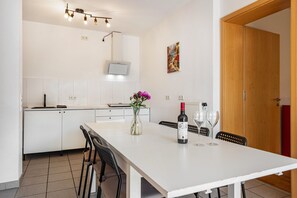 A modern kitchen with white cabinets, a dining table with chairs, a vase with flowers, and a bottle of wine. - Lake Constance Holiday Home Brunnenberg – Relaxation Close to the Lake (Sipplingen)