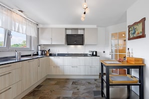 A modern kitchen with light wood cabinets, a black countertop, a built-in oven, and a wooden table with a tray. - Apartment 'Reiselust' with Private Terrace and Wi-Fi (Stockach)