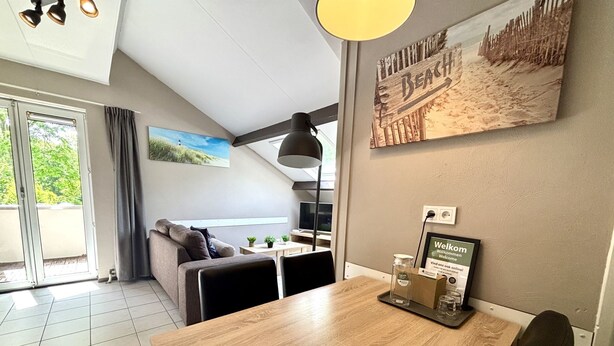 A modern living room with a wooden dining table, a sofa, and a painting of a beach scene. - Boszicht 4 by Interhome (Oostkapelle)