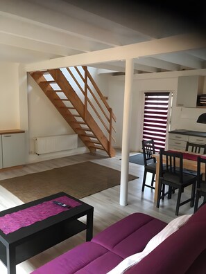 Una sala de estar con un sofá, una mesa de centro, una escalera, una zona de comedor con sillas y una cocina.