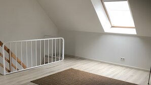 Une pièce aux hauts plafonds, dotée d’une lucarne, d’une rambarde blanche et d’un tapis marron.