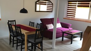 Un coin repas comprenant une table et des chaises, un canapé, une table basse et une fenêtre avec des stores.