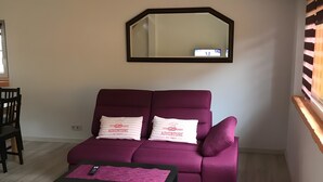 Un salon avec un canapé, une table basse, un miroir et une fenêtre avec des stores.