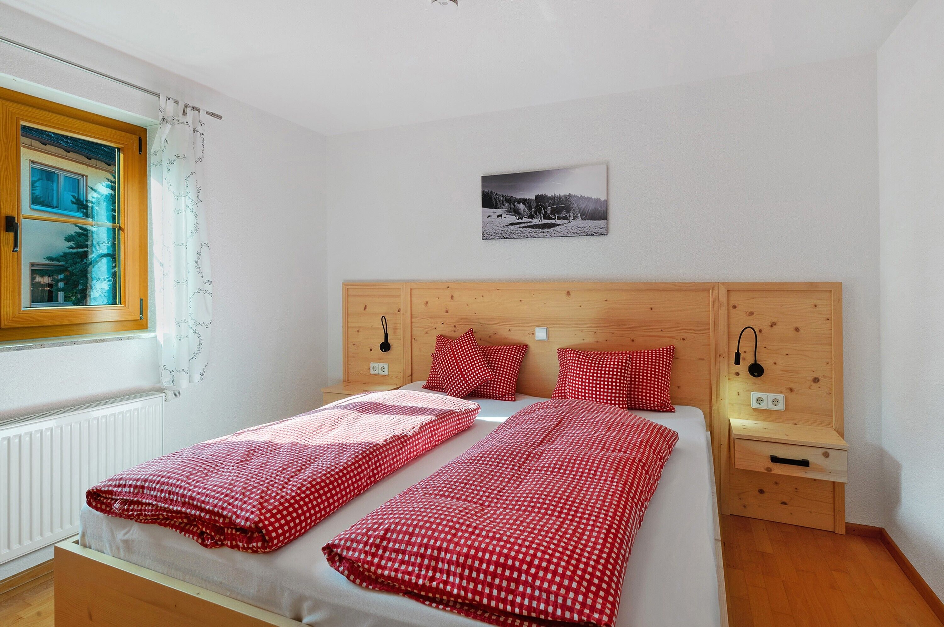 Un dormitorio con dos camas, cabeceros de madera, mesitas de noche, una ventana con cortinas y un cuadro colgado en la pared.