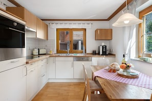 Una cocina moderna con armarios de madera, horno empotrado y comedor con mesa y sillas de madera.
