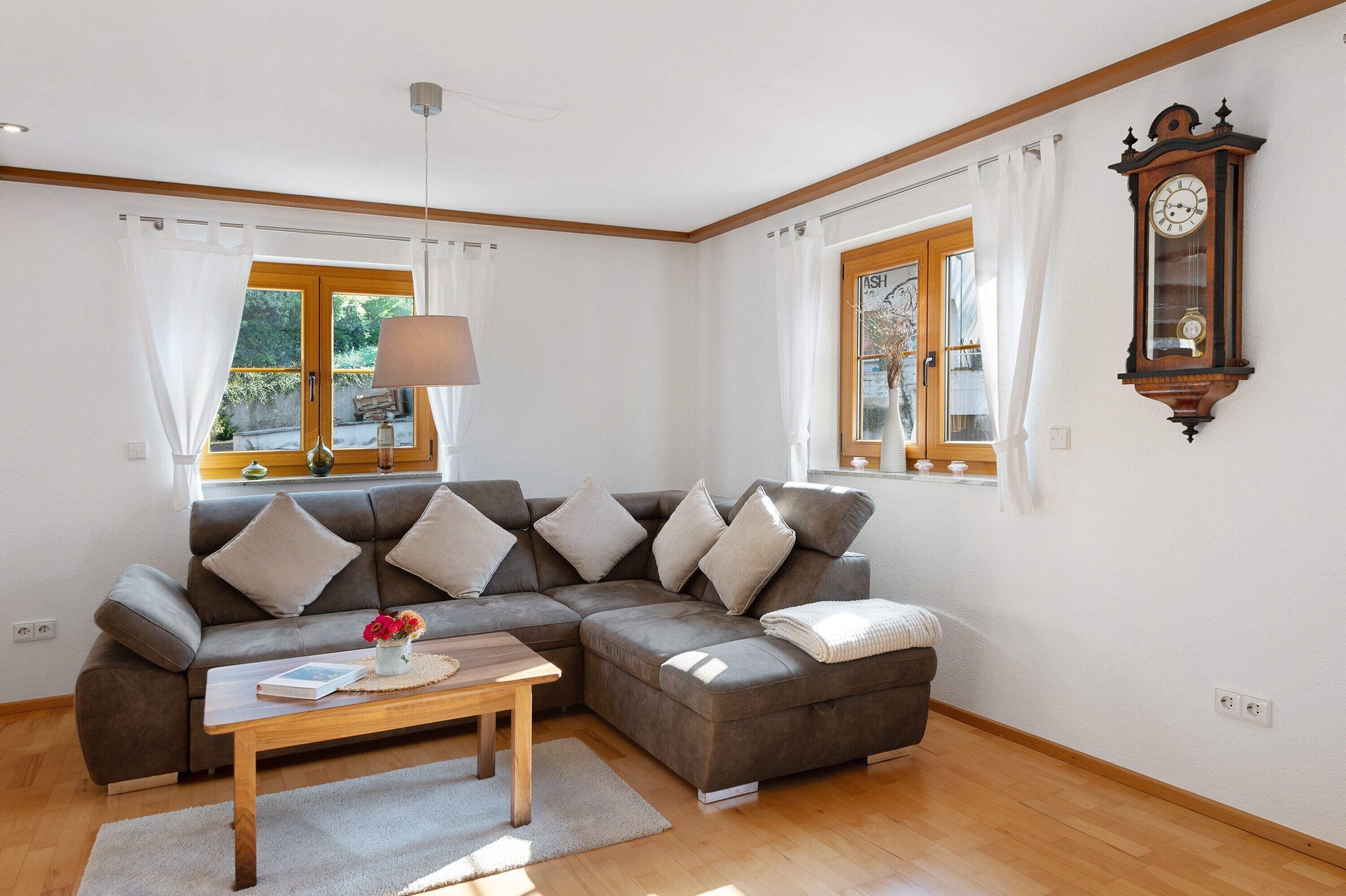 A modern living room with a sectional sofa, a wooden coffee table, and a large wall clock.