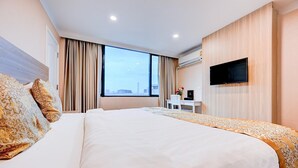 A hotel room with a large bed, a flat-screen TV mounted on the wall, and a window with curtains.