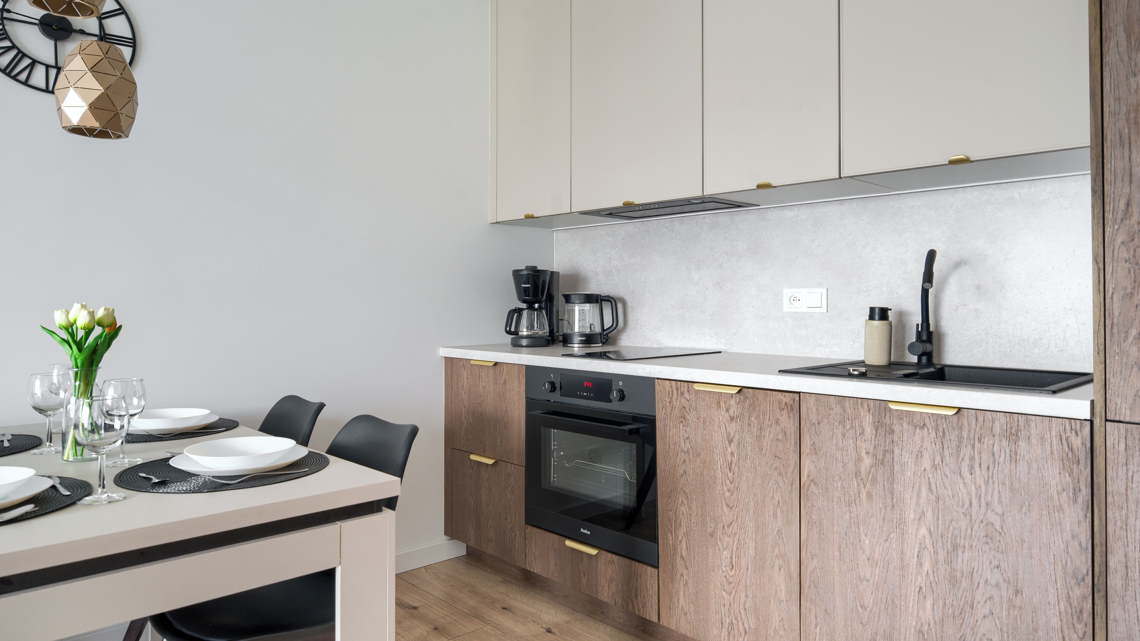 A modern kitchen with a built-in oven, a coffee maker, and a kettle on the countertop.