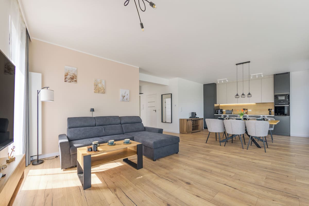 A modern living room with a grey sofa, a wooden coffee table, and a dining area with a table set for four.