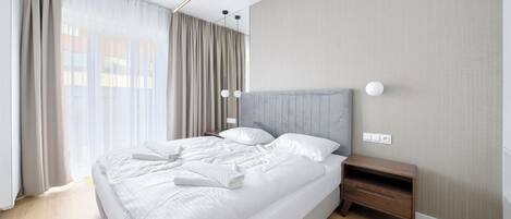 A modern hotel room with a large bed, a wooden nightstand, and a headboard with built-in lighting.