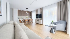 A modern living room with a sofa, a dining area with chairs, a TV, and a kitchen in the background. - Apartamenty Sun & Snow Sand Dunes (Dziwnów)