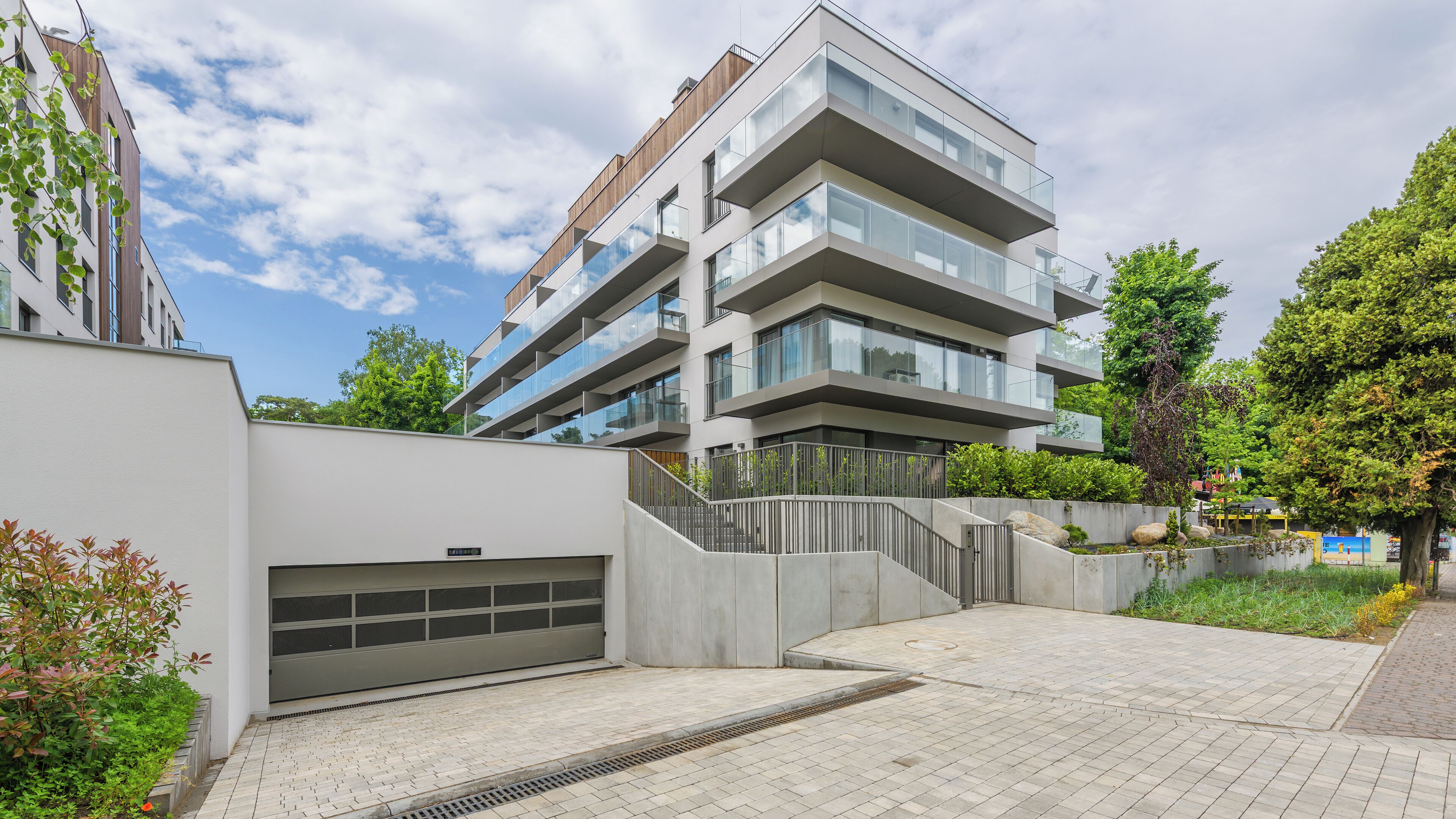 Un immeuble résidentiel moderne à plusieurs étages, doté d’une entrée de garage, d’un escalier en béton et d’une allée pavée.
