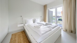 Une chambre à coucher moderne, dotée d’un grand lit, d’une table de chevet et offrant une vue sur l’extérieur grâce à une porte-fenêtre coulissante.