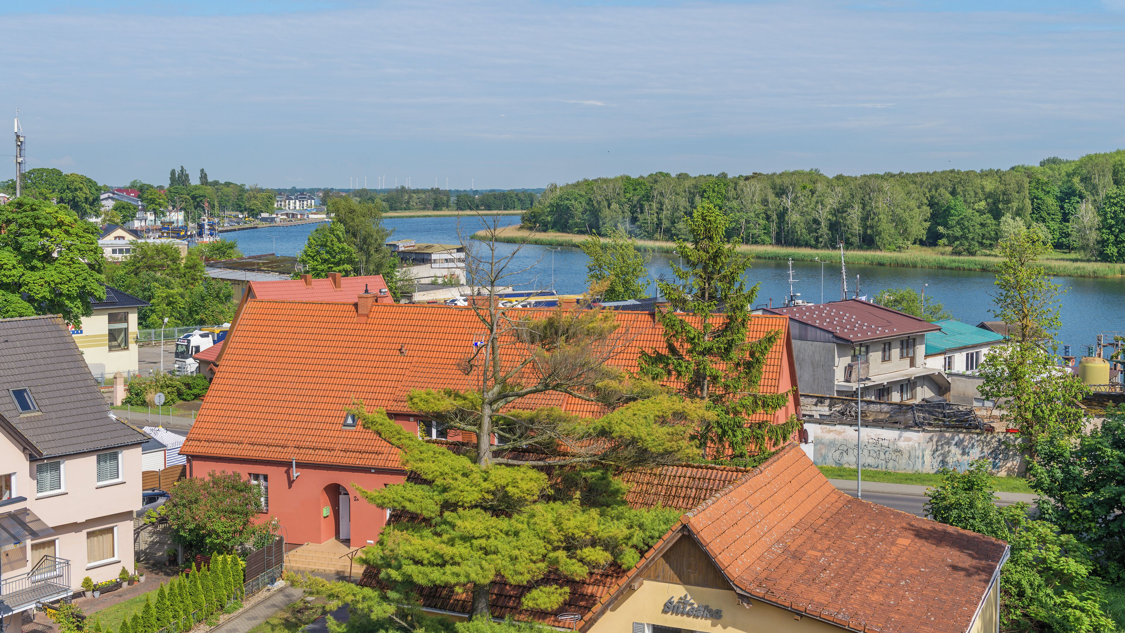 A residential area with houses featuring red-tiled roofs, a river in the background, and a mix of greenery and buildings.