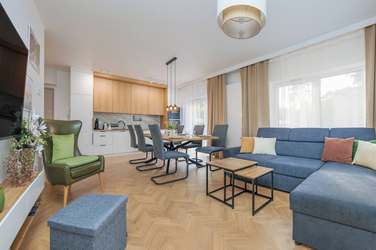 A modern living room with a blue sofa, a green armchair, and a dining area with a wooden table and chairs.