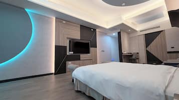 A modern bedroom with a large bed, a flat-screen TV, and a built-in desk with a chair.