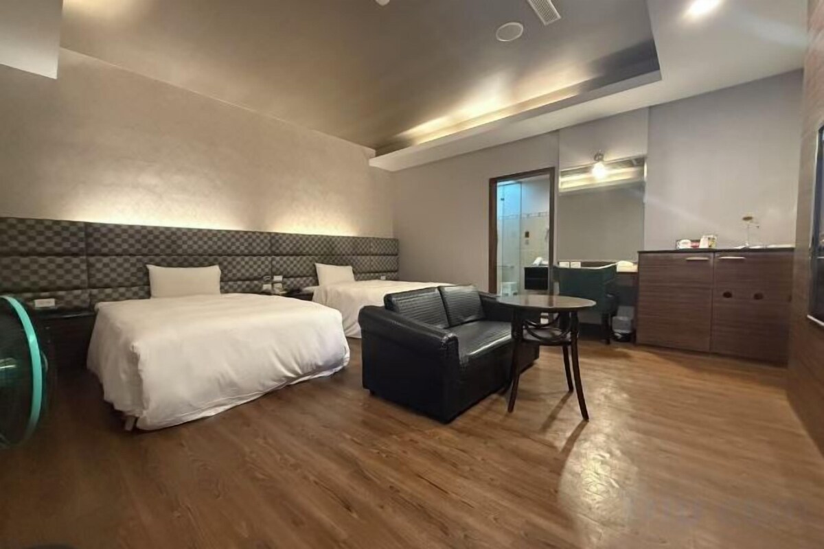 A hotel room with two beds, a sofa, a small table, and a mirror.