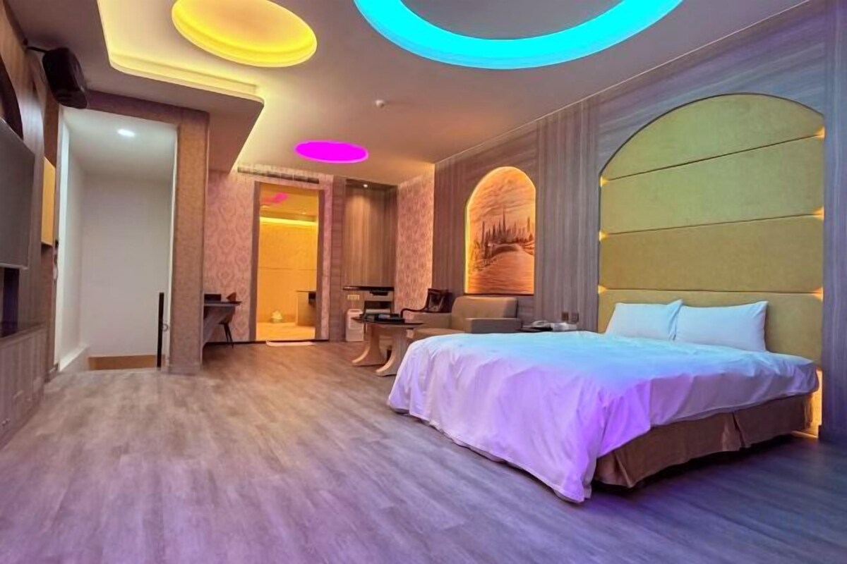 A modern hotel room with a large bed, a vanity with a mirror, and a seating area.