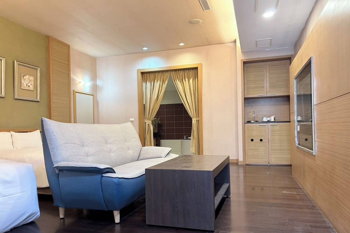 A modern hotel room with a sofa, a small table, and a kitchenette area.