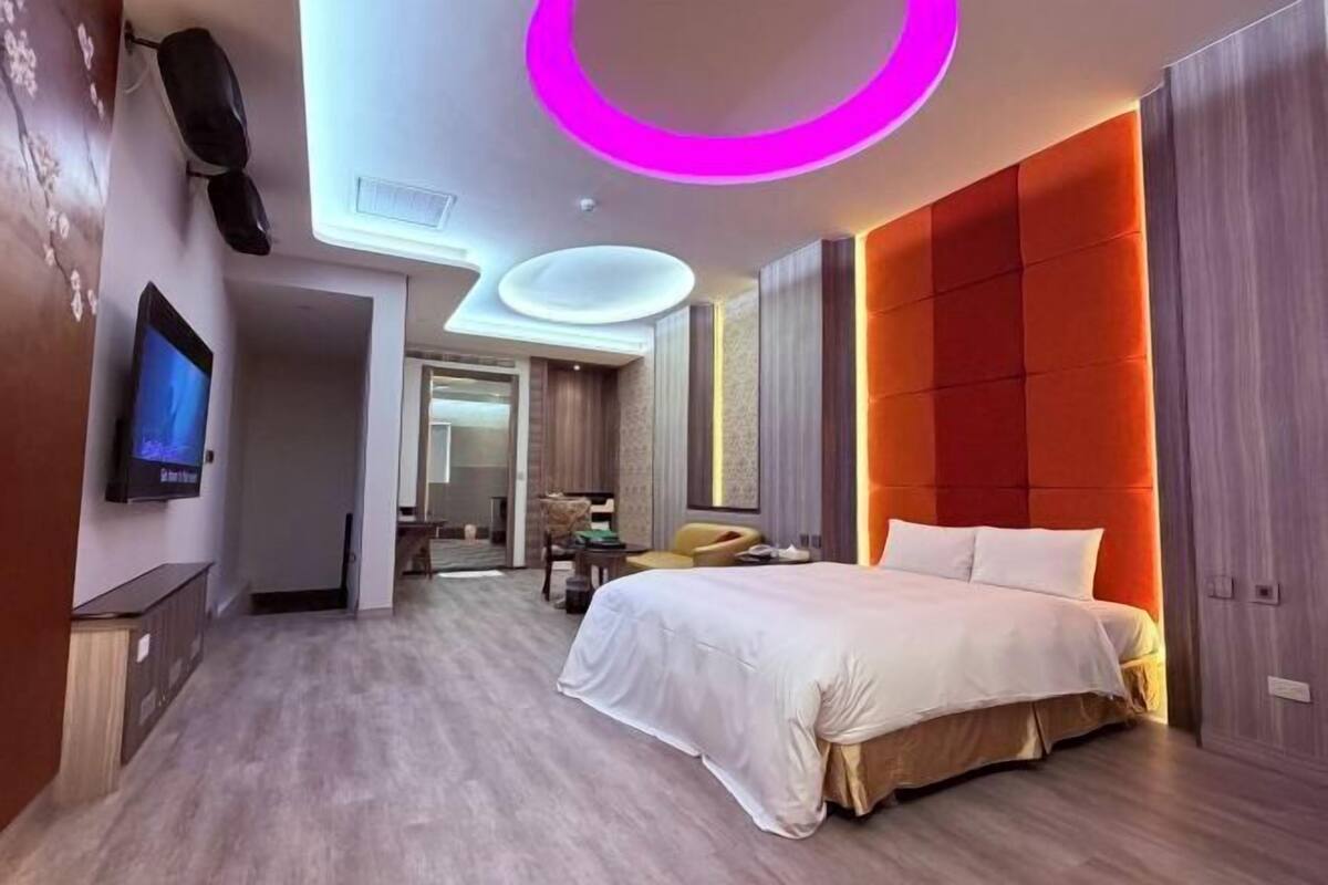 A modern hotel room with a bed, a television, and a circular ceiling light.