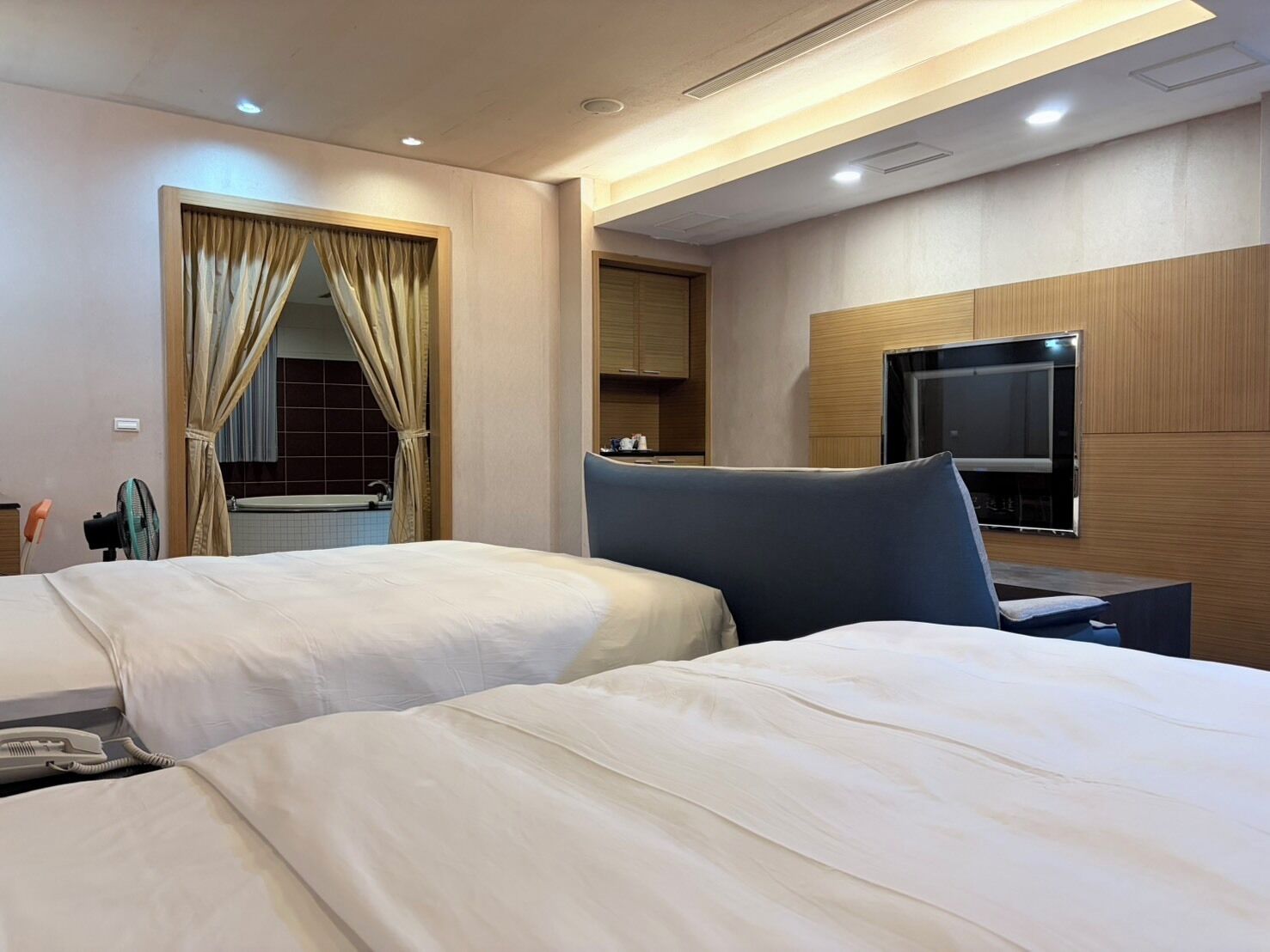 Habitación de hotel con dos camas, un televisor, un escritorio y un baño visible a través de una cortina.