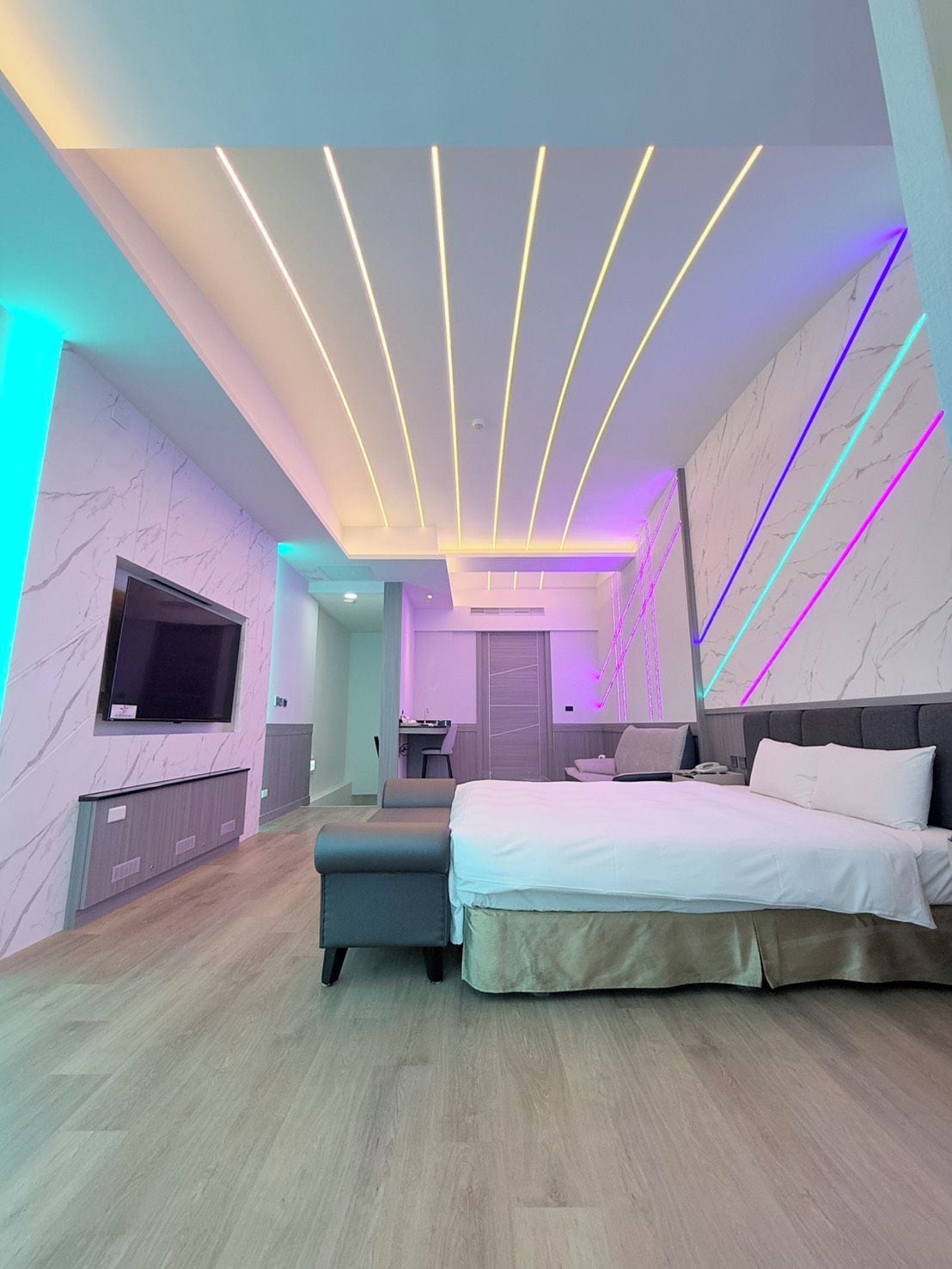 A modern bedroom with a bed, seating area, and a TV.