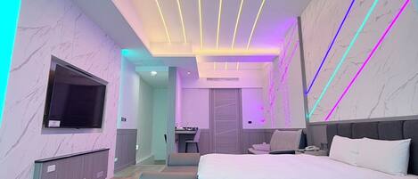 A modern bedroom with a bed, seating area, and a TV.
