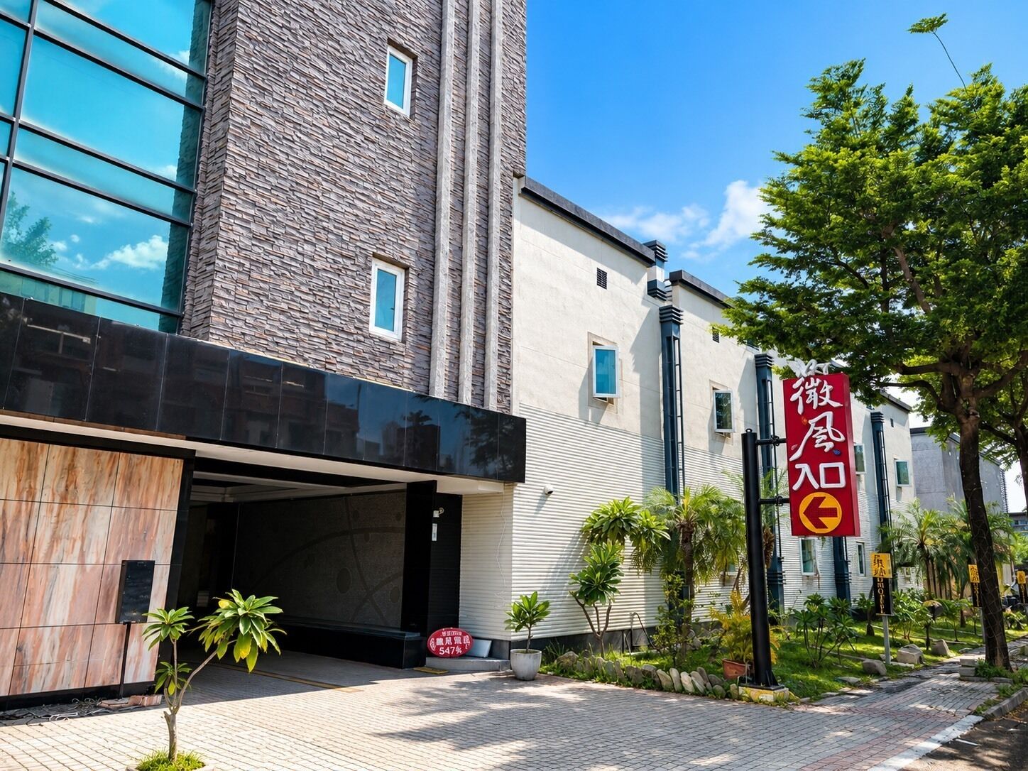 A hotel entrance with a modern facade, a stone tower, and a red sign with Chinese characters.