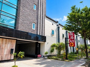 A hotel entrance with a modern facade, a stone tower, and a red sign with Chinese characters. - Lisa motel (Kaohsiung)