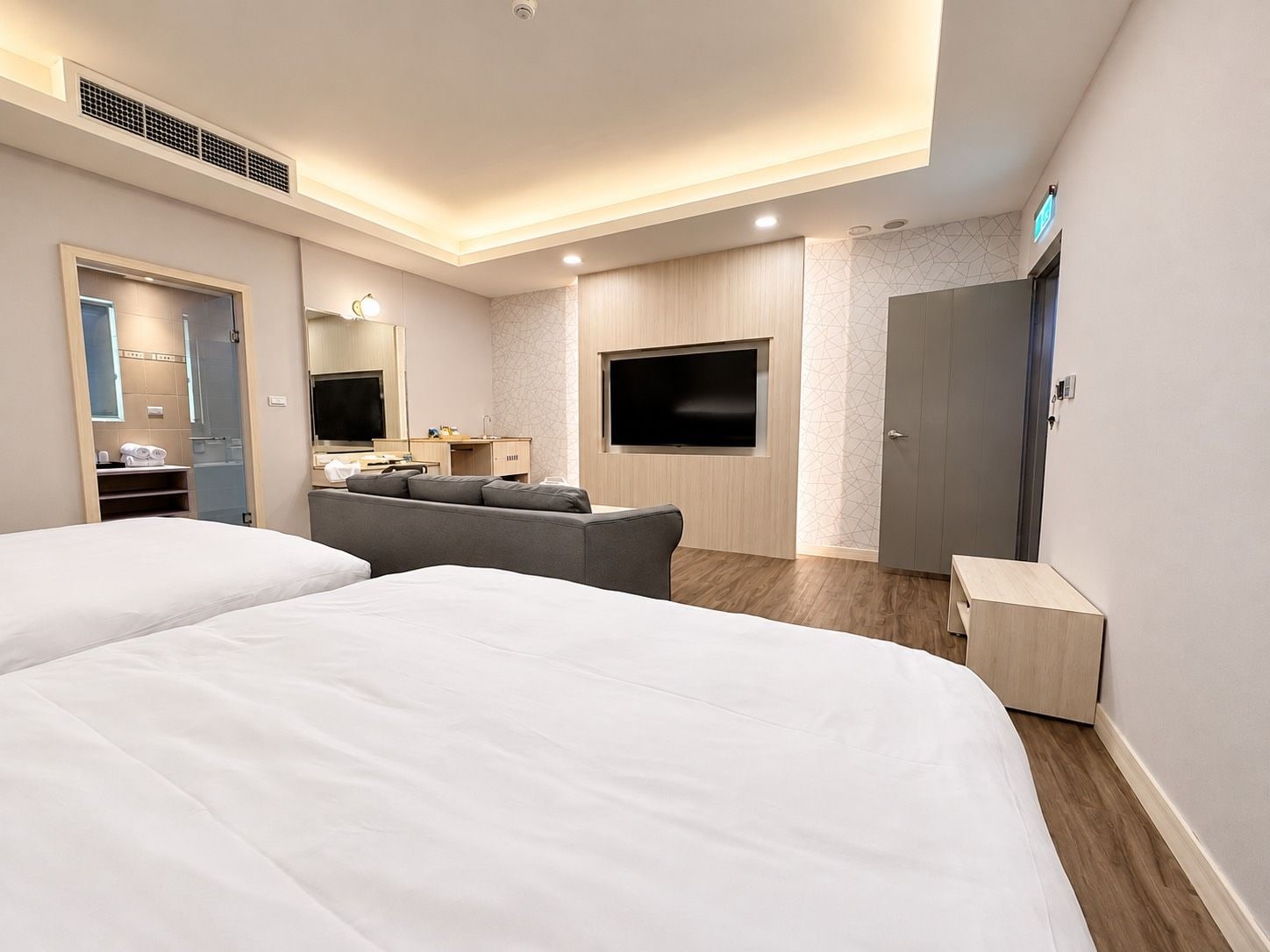 A hotel room with two beds, a sofa, a TV, and a desk.