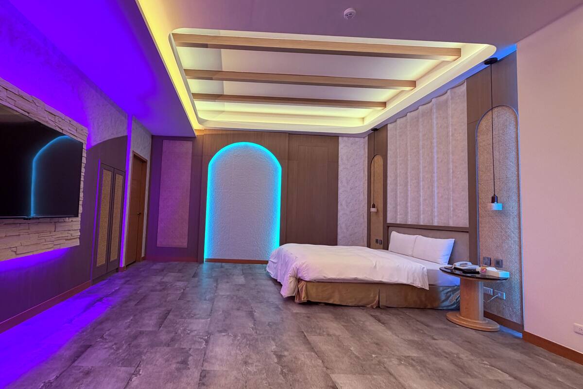 A modern hotel room with a large bed, a flat-screen TV mounted on the wall, and a unique ceiling design.