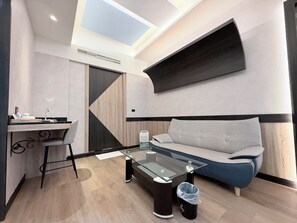 A modern living space with a glass coffee table, a sofa, a desk with a chair, and a built-in air conditioning unit. - Lisa motel (Kaohsiung)