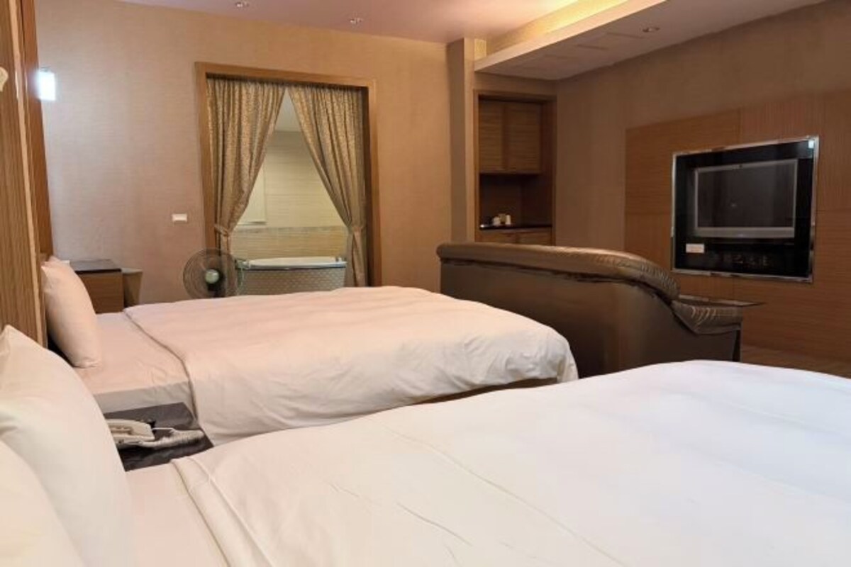 Habitación de hotel con dos camas, televisión, escritorio y ventana con cortinas.