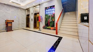 Un vestíbulo de hotel con suelo de mármol, una recepción, una escalera y un adorno floral en la pared.
