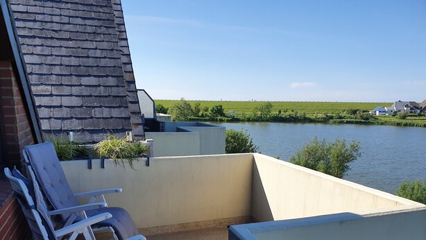 A balcony with chairs and a table overlooking a river. - Holiday Apartment 'Watt'n Utsicht' with Sea View, Balcony and Wi-Fi (Nordstrand)