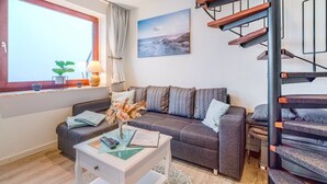 A modern living room with a sofa, a coffee table, a lamp, a painting, and a staircase. - Holiday Apartment 'Watt'n Utsicht' with Sea View, Balcony and Wi-Fi (Nordstrand)