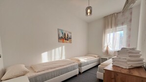 Une chambre avec deux lits simples, une petite table avec des serviettes, un luminaire suspendu et un tableau représentant un paysage urbain accroché au mur.
