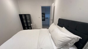 A neatly made bed with white linens, a dark headboard, and a bedside table with a lamp. - Excel London Newly Built Charming 2 bedroom apartment (London)