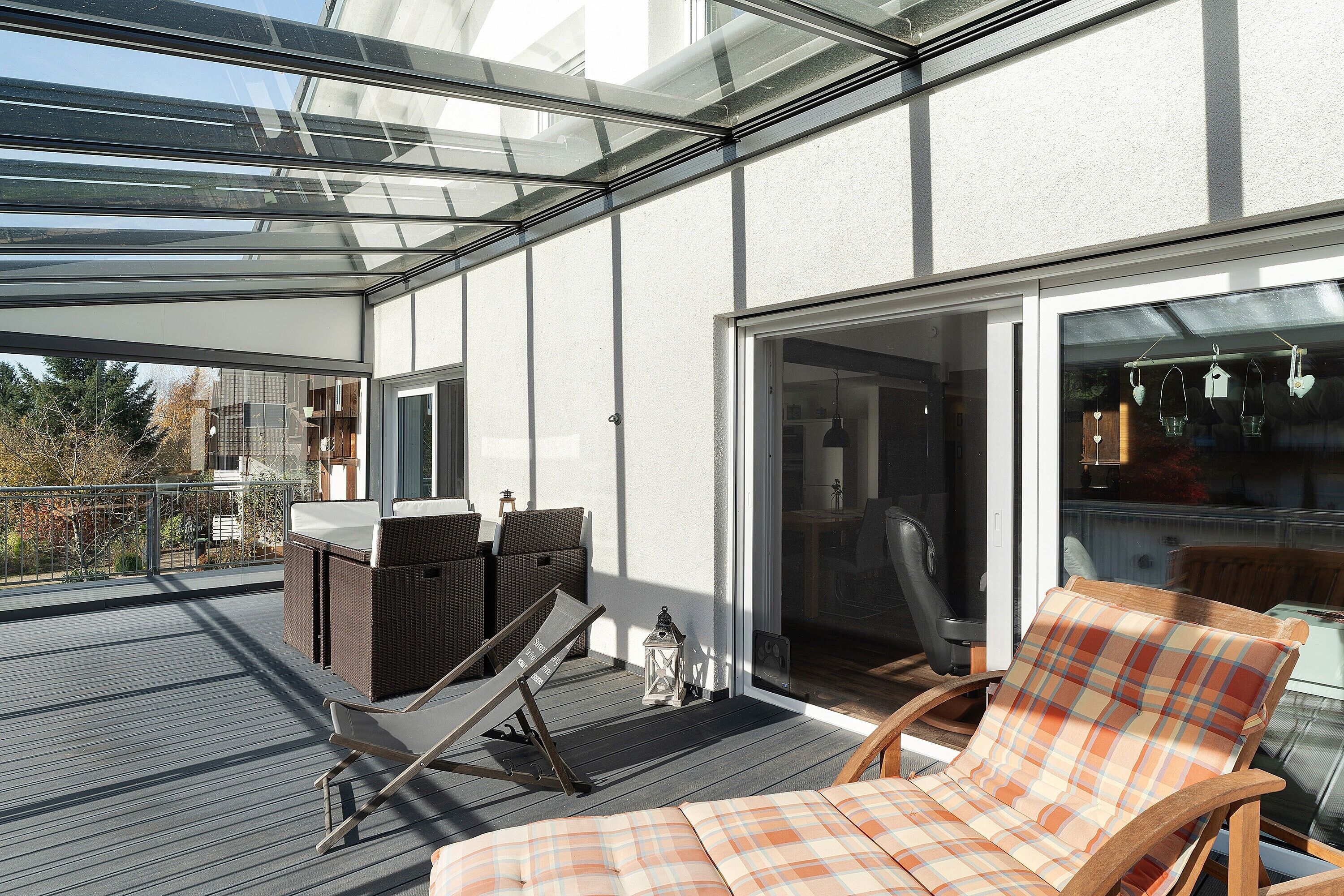Eine überdachte Terrasse mit einer Liege, einem kleinen Tisch und einem Korbsessel.
