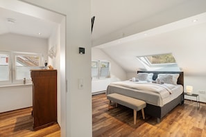 A bedroom with a sloped ceiling, a skylight, a bed with pillows, a bedside table, and a wooden cabinet. - Holiday Apartment 'Forest' with Private Terrace and Wi-Fi (Renchen)
