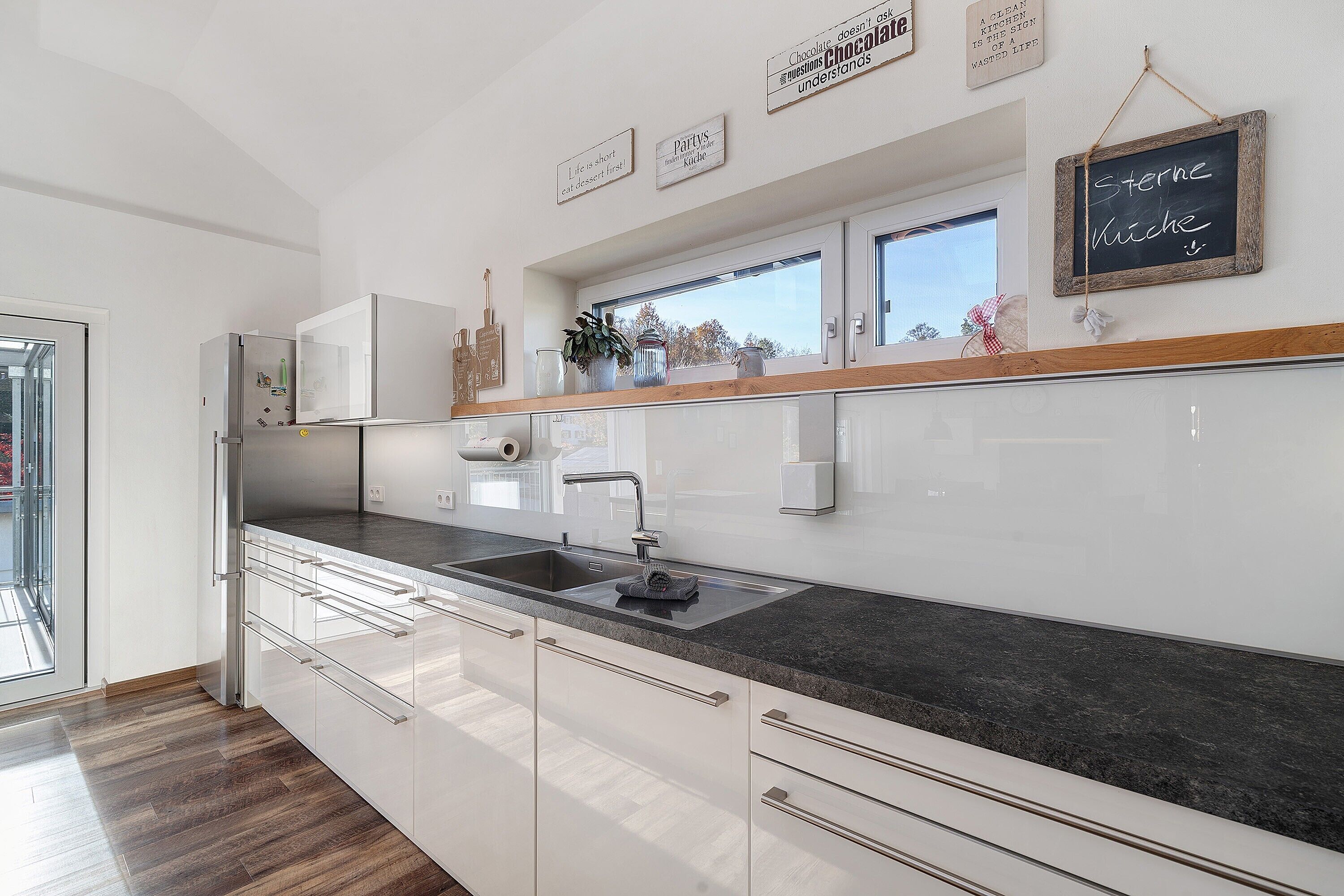 A modern kitchen with white cabinetry, a black countertop, and a window above the sink.