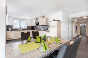 Una cocina moderna con armarios de madera, una mesa de comedor con servilletas verdes y vistas al cuarto contiguo.