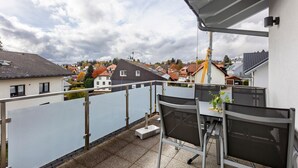 Un balcon avec une table et des chaises, une vue sur des maisons et un ciel nuageux.
