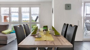 Un espace repas avec une table en bois, des chaises noires et une vue dégagée grâce à de grandes fenêtres.
