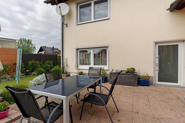 A patio with a glass table and chairs, surrounded by potted plants and a small garden.